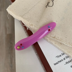 Detail of a purple acrylic hair clip with colorful rhinestones on a fabric background