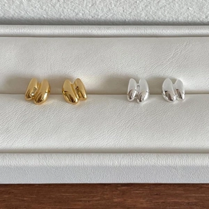 Minimalist gold and silver pea-shaped metal stud earrings on a beige jewelry display