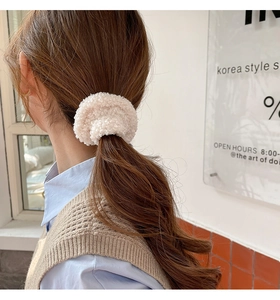Detail of soft cream faux shearling scrunchie styled on a woman's low ponytail
