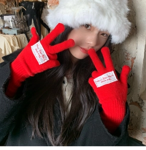 Detail of red knitted gloves with white embroidered French text patch worn by a model