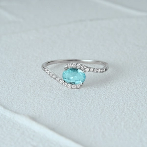 Macro shot of silver ring with light blue oval gemstone and twisted pavé diamond band