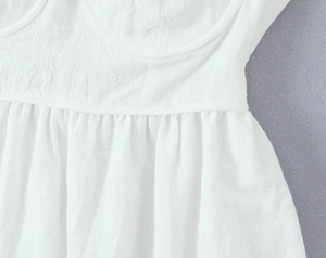 Detailed macro view of white lace dress pleated waist seam and textured fabric finish