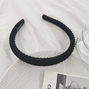 Detail shot of black twisted fabric headband with handmade label on white textured background