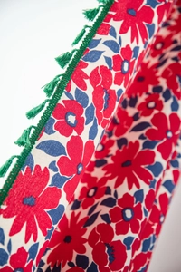 Detailed close-up of red floral print cotton linen curtain with green tassel trim edge