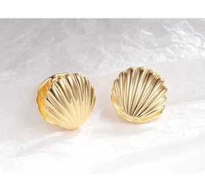 Detailed close-up of golden shell-textured earrings on a minimalist white paper background