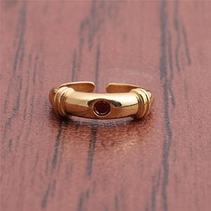Close-up of golden geometric open ring with red gemstone and ribbed details