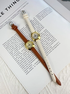 Flat lay of brown and beige leather quartz watches with Roman numeral dials on an open book