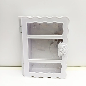 Close-up of a white book-shaped jewelry box with transparent glitter windows and rose decor