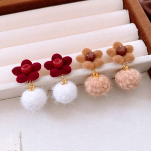 Detail of floral velvet earrings with soft pompom charms in burgundy and beige colors