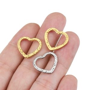 Hammered texture heart pendants in gold and silver held to show actual product size
