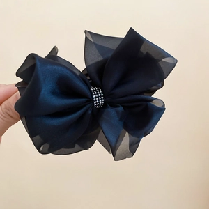 Dettaglio molletta per capelli con fiocco in organza nera e strass su sfondo beige