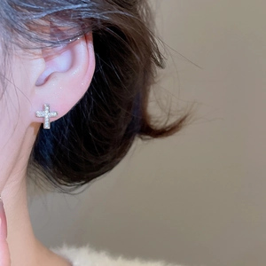 Close-up of a silver zircon cross stud earring worn by a model in soft lighting