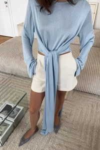 Dettaglio maglia a maniche lunghe azzurra con fiocco decorativo in vita