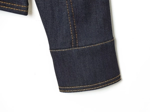 Gros plan du poignet d'une veste en jean bleu foncé avec surpiqûres jaunes contrastées