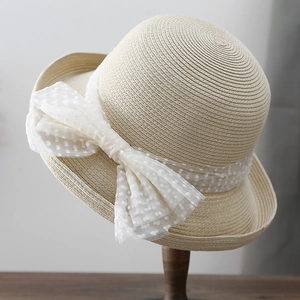 Détail d'un chapeau de paille beige tissé avec un grand nœud en dentelle à pois blancs