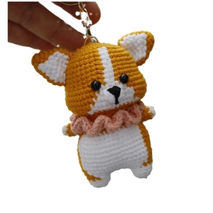 Handmade crochet corgi dog keychain in yellow and white yarn with pink collar on white background