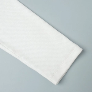 Detailed close-up of white ribbed knit fabric and high-quality flatlock stitching on the cuff