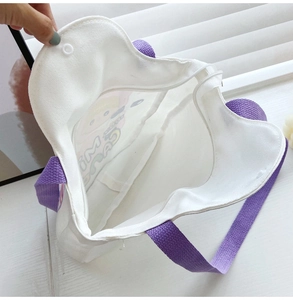 Detail of white canvas tote bag showing purple woven strap, zipper, and spacious interior