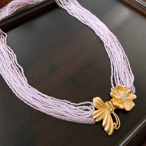 Détail d'une chaîne de corps en perles roses avec fermoir fleur et papillon doré
