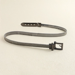 Detail view of a gunmetal spring metal belt with a square buckle on a beige background