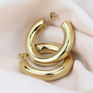 Macro view of chunky golden hoop earrings resting on pink silk fabric background