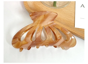 Detailed close-up of amber tortoiseshell cellulose acetate hair claw clip on wooden tray
