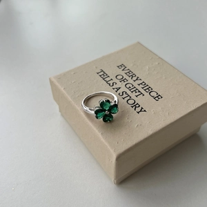 Close-up of S925 silver four-leaf clover ring with green zircon on a textured gift box