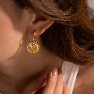 Detailed close-up of 18K gold plated hoop earrings with star and moon relief patterns