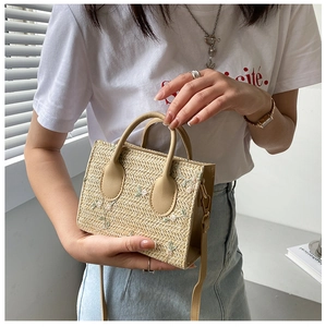 Detail view of beige straw handbag featuring delicate flower embroidery and leather handles