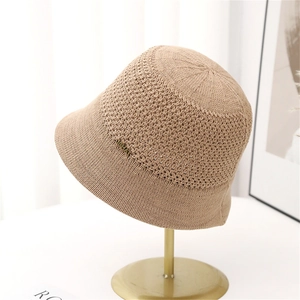Beige crochet knit bucket hat with metal emblem on display stand for women