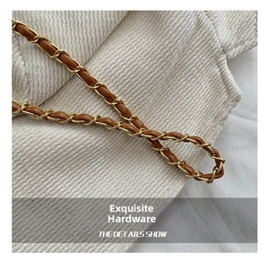 Detailed macro view of woven gold metal chain and brown leather strap on a bucket bag