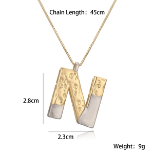 Detail showing two-tone gold and silver N-letter pendant with hammered texture and size info