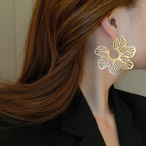 Close-up of model wearing large hollow gold flower stud earrings in a professional setting