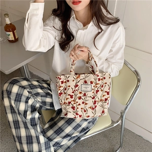 Corduroy tote bag with floral patterns held by a model in a cozy cafe setting
