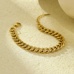 Macro view of gold plated Cuban chain bracelet with lobster clasp on textured background
