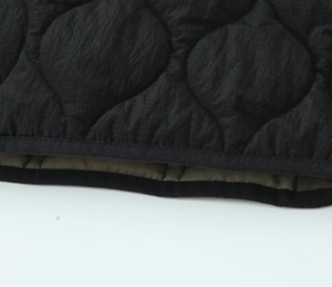 Detail of black quilted jacket with olive green lining and wave stitching craftsmanship