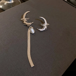 Detail of silver asymmetric moon earrings with blue cat-eye stone and long snake chain tassel