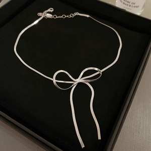 Close-up of silver bow pendant snake bone chain necklace in black velvet gift box
