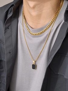 Detail of men's gold Cuban chain layered with a black rectangular pendant necklace