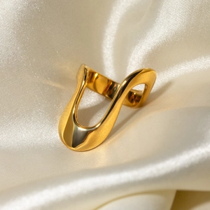 Artistic golden irregular wavy sculpture ring on elegant beige silk fabric background