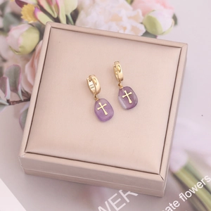 Boucles d'oreilles dorées avec gouttes violettes et croix dans un coffret cadeau