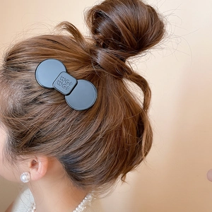 Close-up of matte black resin hair clip with letter engraving on elegant bun hairstyle