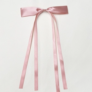Detail of pink satin bow hair clip with long flowing ribbons on white background
