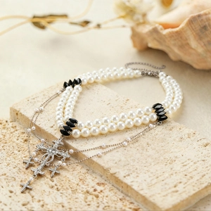Detailed view of layered faux pearl sweater chain with rhinestone-encrusted silver crosses