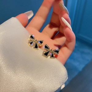 Detail of gold bow earrings with black inlay and sparkling crystals held by a hand
