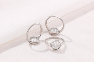 Dettaglio di tre anelli in argento S925 con motivi geometrici e farfalla su tessuto bianco