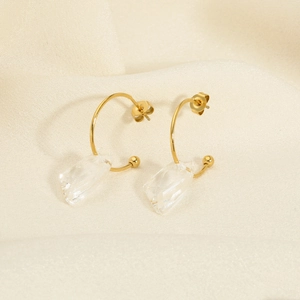 Detail of gold C-shaped hoop earrings with irregular clear crystal pendant on silk fabric