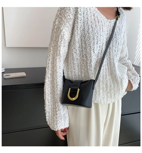 Detail of minimalist black crossbody bag with polished gold U-shaped metal buckle clasp