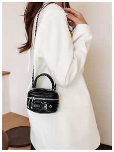 Detailed side view of black quilted cylinder crossbody bag with chain strap and handle