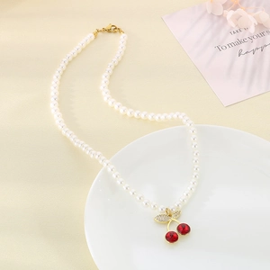 Handmade red cherry pendant necklace with white pearls and gold accents on a white plate